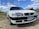 A white sedan car is parked on a gravel surface under a partly cloudy sky. The vehicle has a sleek design with prominent headlights. Its front license plate reads UG-43 88, with Chile indicated as the location.
