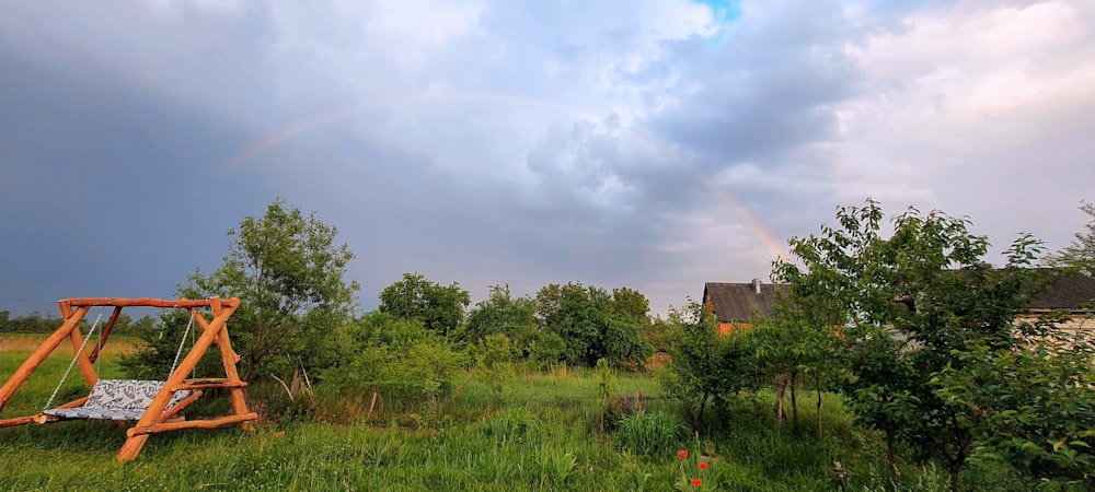 a wooden swing in a field with a rainbow in the background