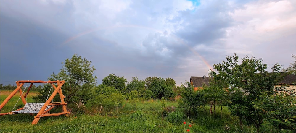 eine Holzschaukel auf einem Feld mit einem Regenbogen im Hintergrund