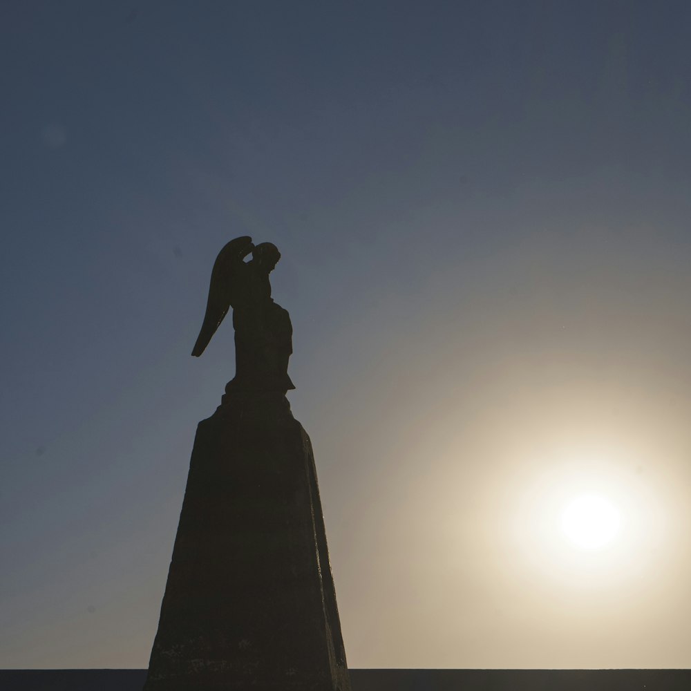 a statue of a person holding a bird with the sun in the background