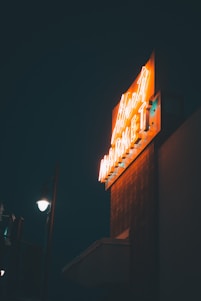 A skilled craftsman installing a glowing neon box sign on a storefront at dusk.