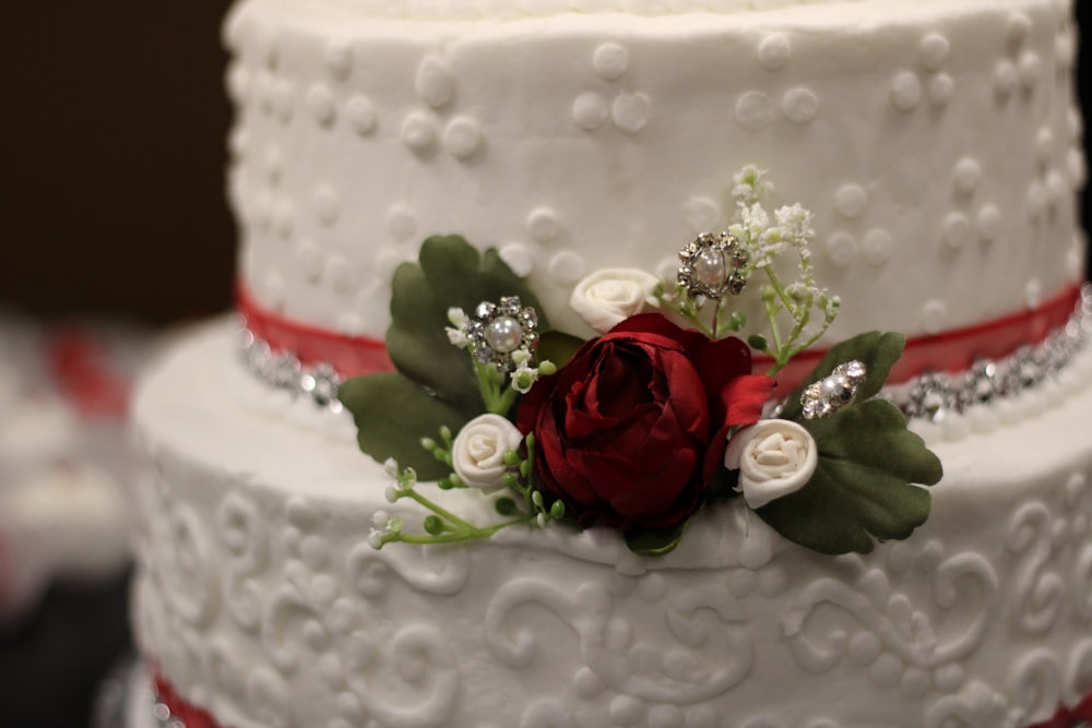 a three tiered wedding cake with a red rose on top