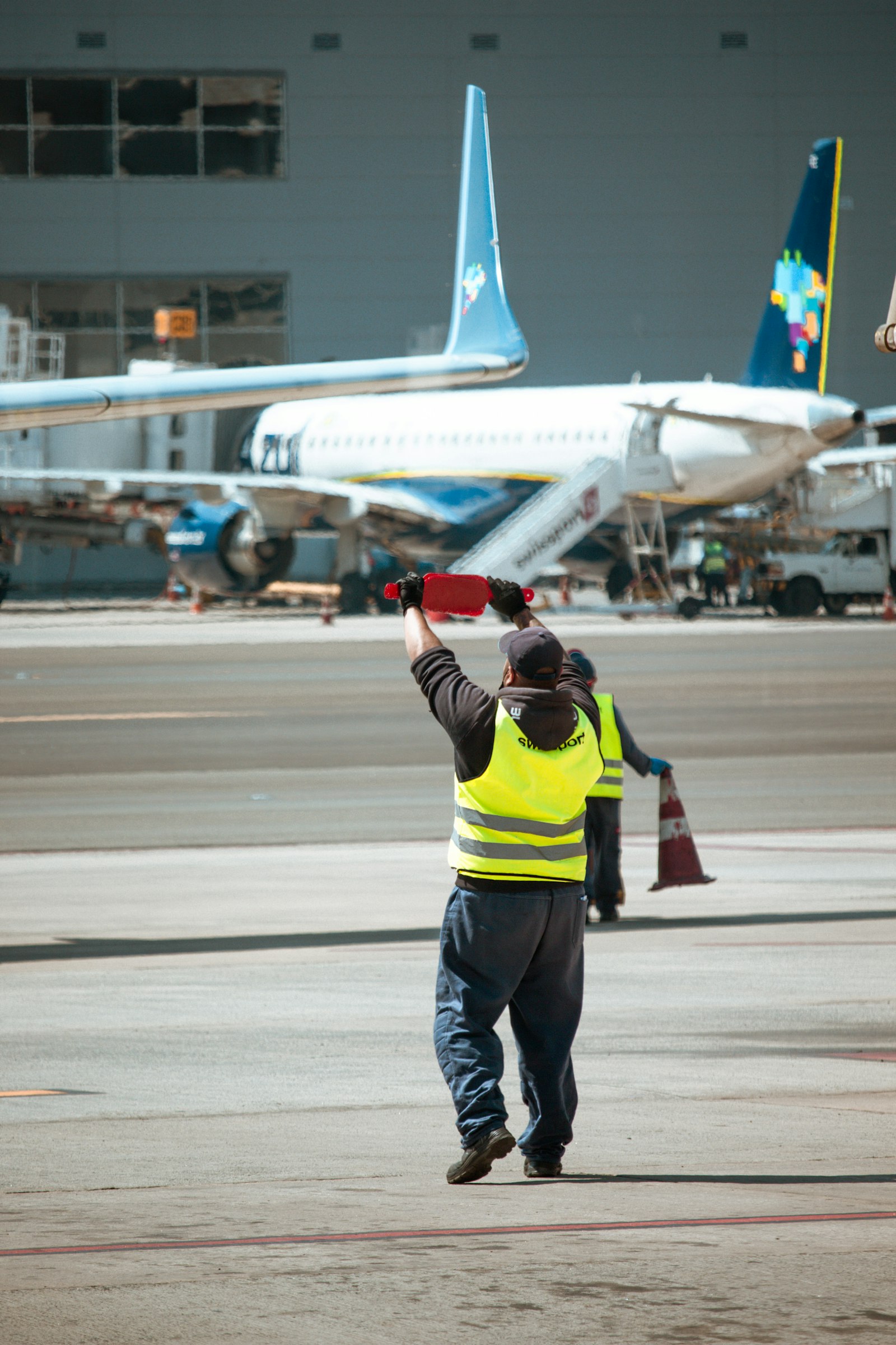 Airport ramp worker in a high-visibility vest walking toward a parked aircraft on sun-baked tarmac, the working environment where ramp agents face radiant pavement heat, APU exhaust, and no shade during summer banks