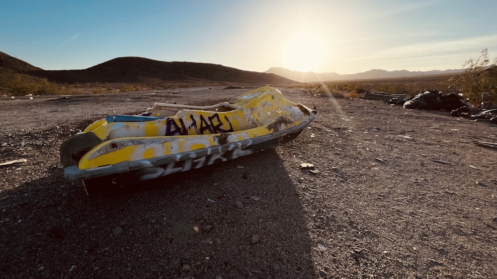 a yellow and white boat sitting on top of a dirt field