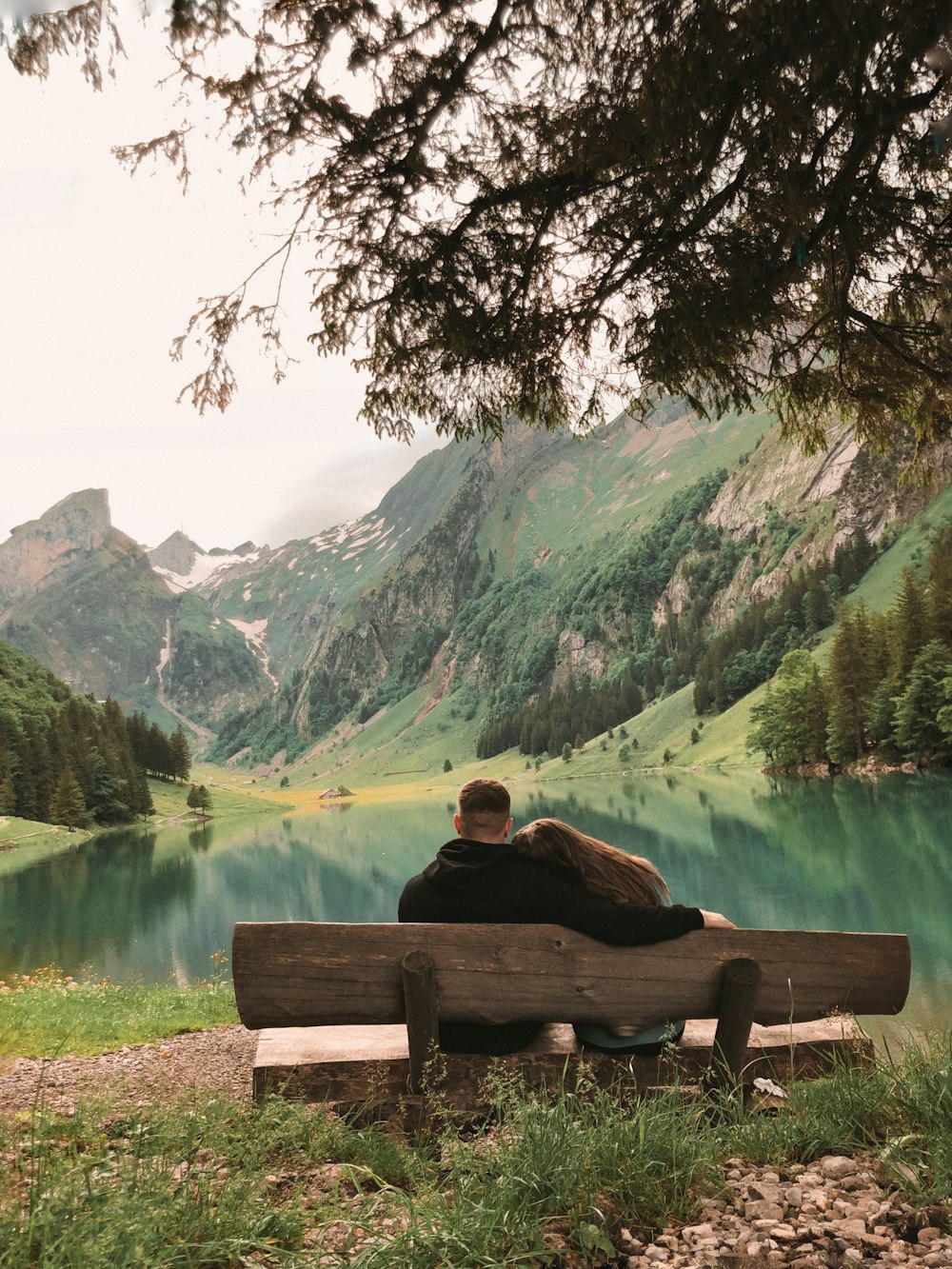 a man and a woman sitting on a bench in front of a lake