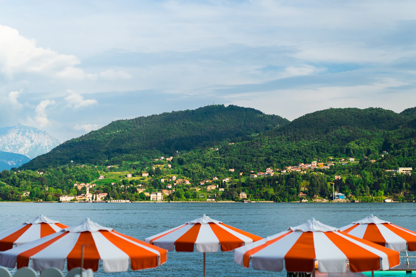 Orange and white striped umbrellas on a lido beside Lake Como, mountains behind