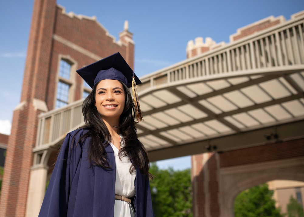 a woman in a cap and gown standing in front of a bridge