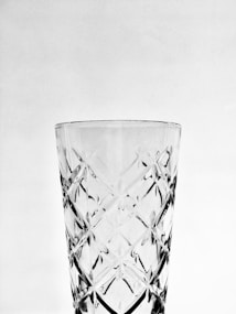 A transparent glass with intricate cut patterns is centered against a plain background. The surface features crisscross diamond shapes, enhancing its elegance and complexity.
