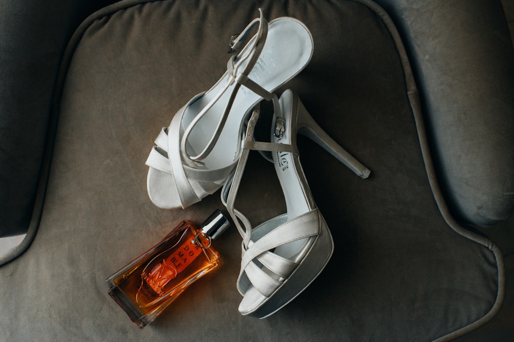 a pair of white high heeled shoes next to a bottle of perfume