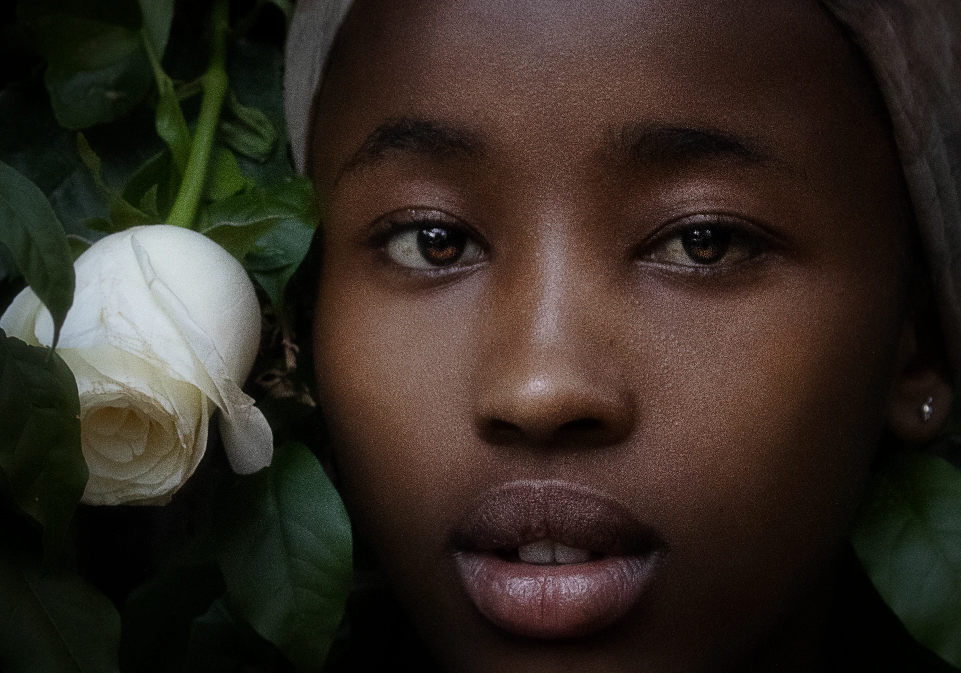 A close-up portrait of a person framed by lush greenery, their expression telling a quiet story.