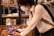 A person wearing a white shirt, tie, and surgical mask uses a stylus on a tablet device. They have a gray backpack and are in an interior space with shelves filled with books or similar items in the background.