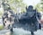 A large, intricately designed metal sculpture of a mythical creature with a lion-like body, thick mane, and decorative patterns on its back. The sculpture is set outdoors in a park-like area surrounded by trees and greenery.