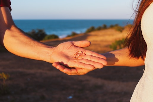 a man and a woman holding hands with the ocean in the background