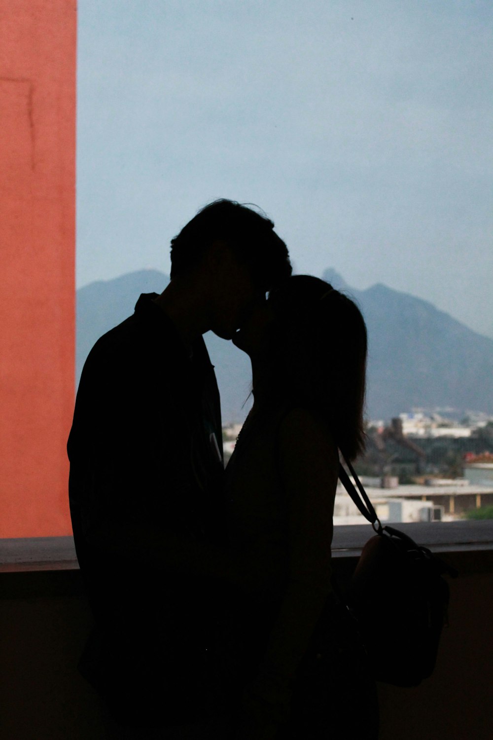 a man and a woman kissing in front of a window