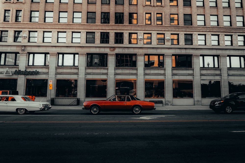 a red car driving down a street next to a tall building