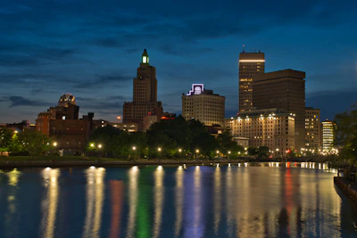 A minimalist cityscape at dusk, with glowing windows and a calm river reflecting the skyline.