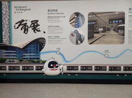 A wall advertisement in a transit area showcases station features and services. The design includes visuals of a train and station, with detailed text in both Chinese and English. A cute cartoon character is present alongside graphics illustrating key highlights.