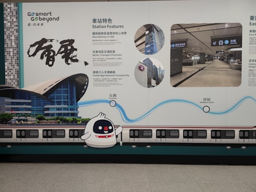 A wall advertisement in a transit area showcases station features and services. The design includes visuals of a train and station, with detailed text in both Chinese and English. A cute cartoon character is present alongside graphics illustrating key highlights.