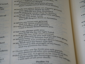 The image displays a close-up view of an open book with text printed in columns. The text is clearly formatted in verses, resembling a page from a Bible. The numbers preceding each line suggest scripture references.