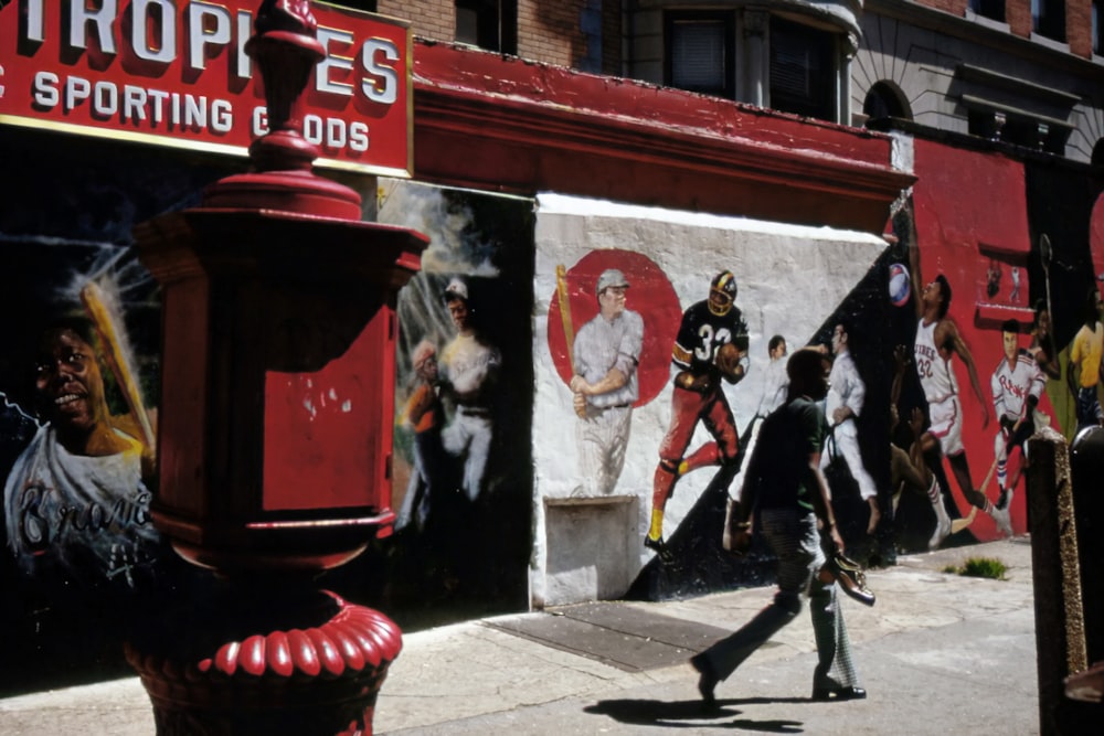 a man walking down a street next to a red fire hydrant