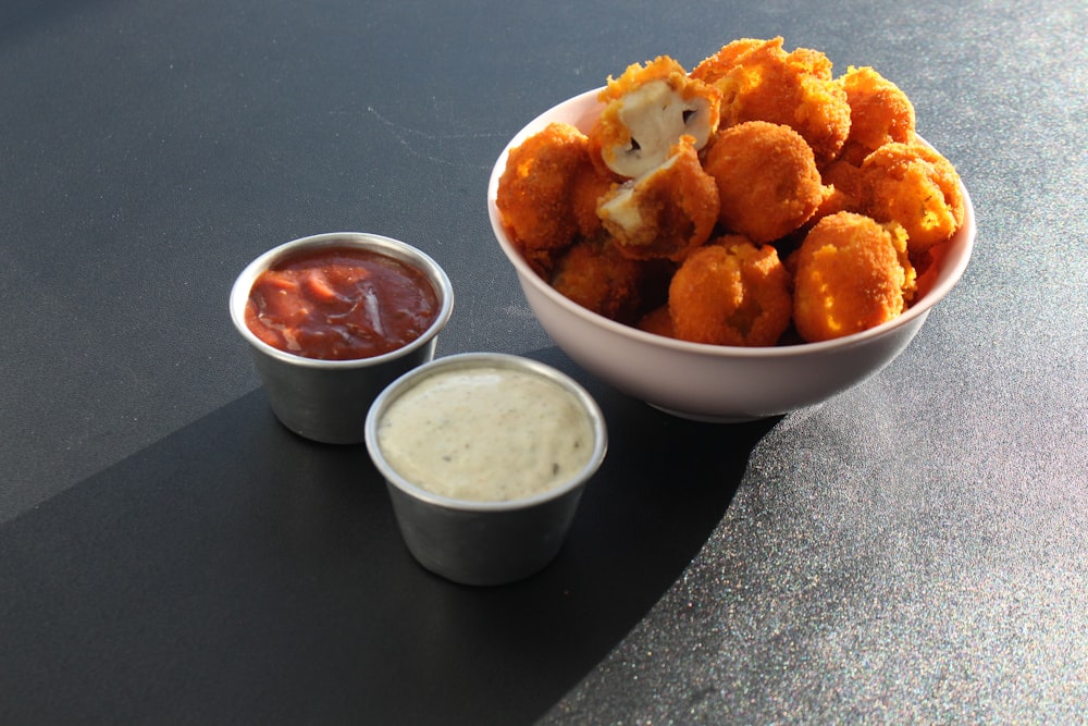 a bowl of tater tots next to a bowl of dipping sauce