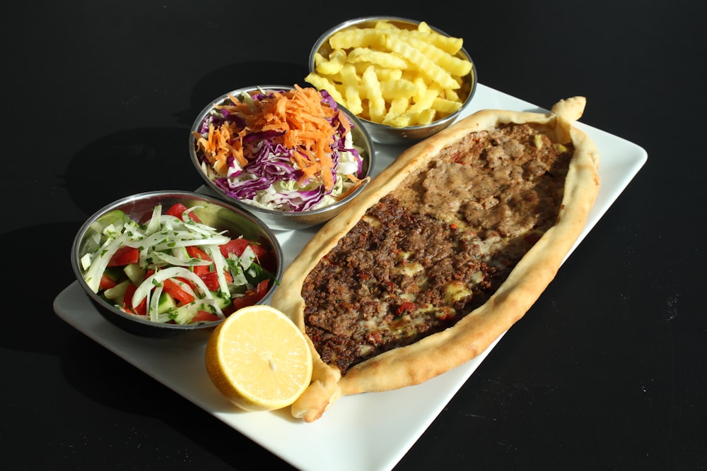 a white plate topped with a meat filled pastry next to bowls of salad and fries