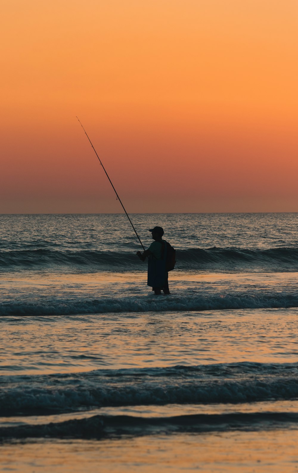 a man fishing in the ocean at sunset