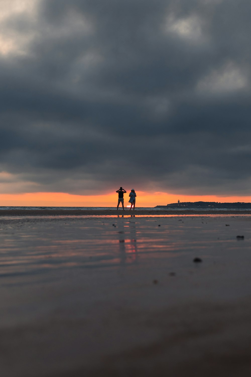 um par de pessoas em pé no topo de uma praia sob um céu nublado