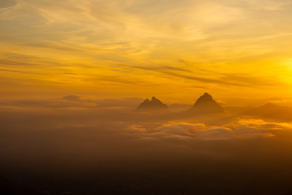 the sun is setting over the mountains above the clouds