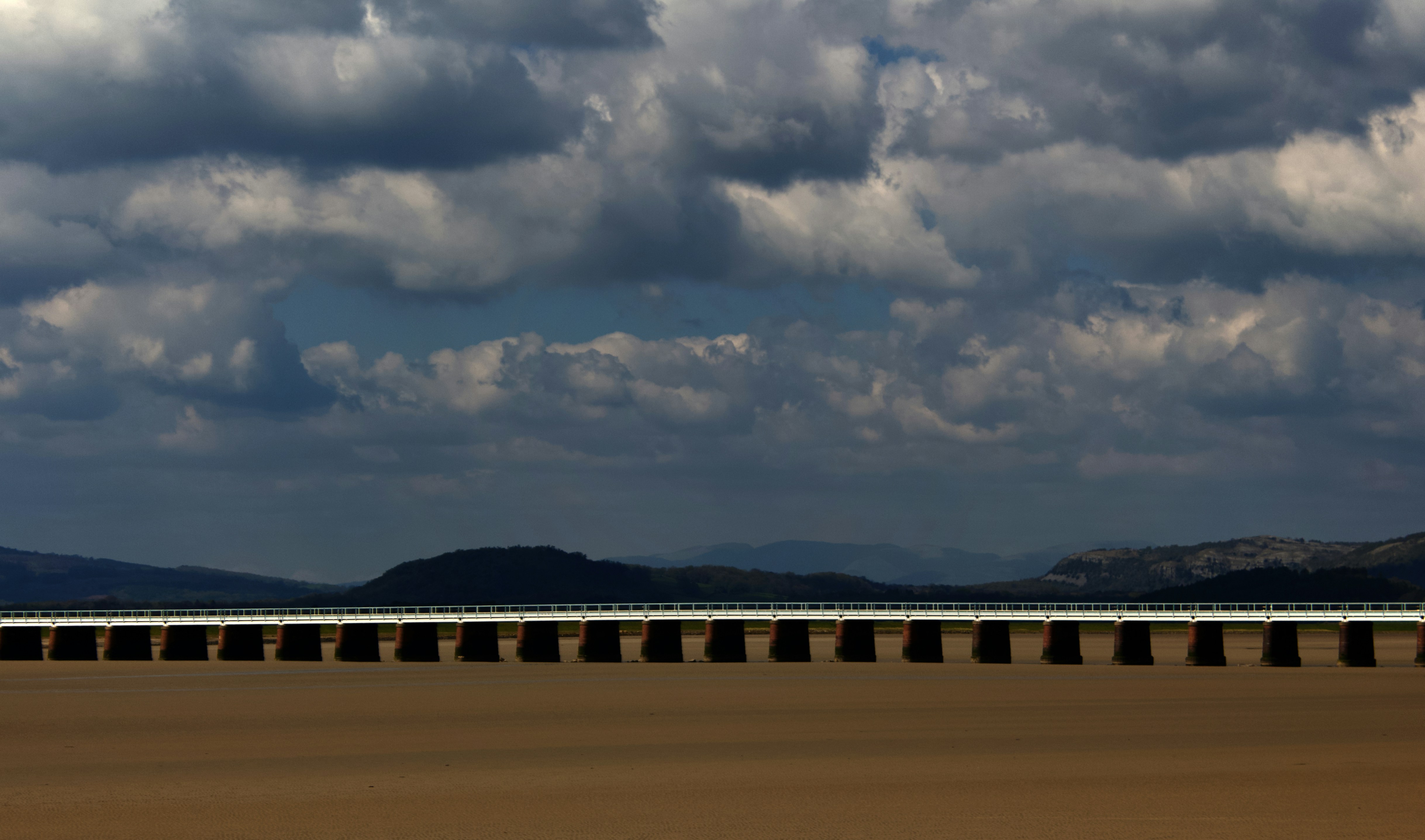 a train traveling across a sandy beach under a cloudy sky