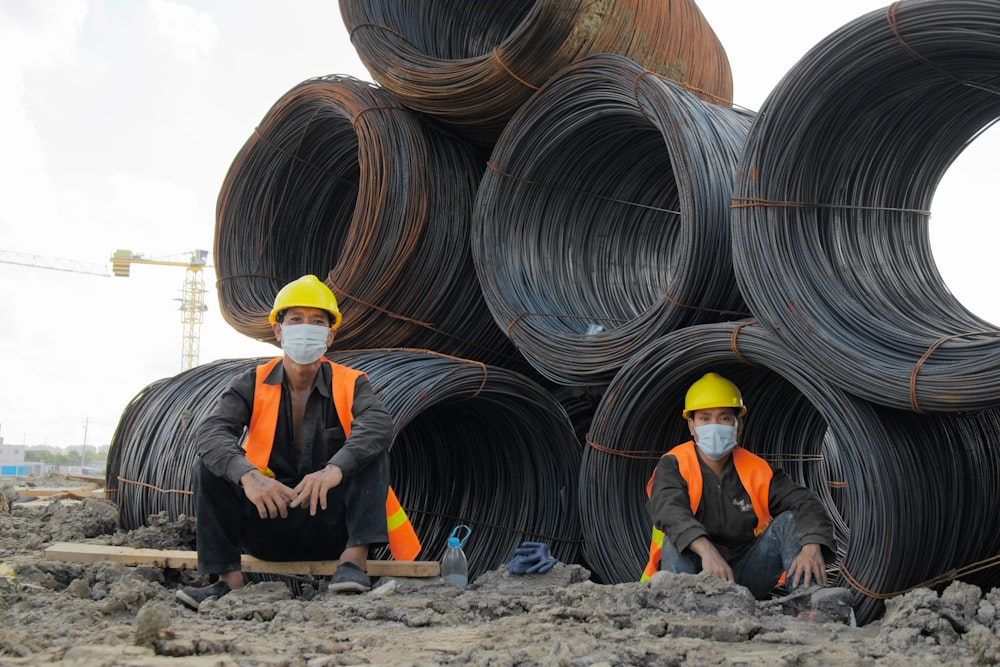 two men in safety gear sitting on a pile of pipes