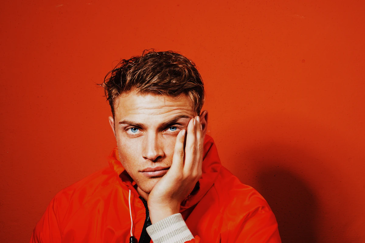 Man in an orange shell jacket posing against an orange backdrop