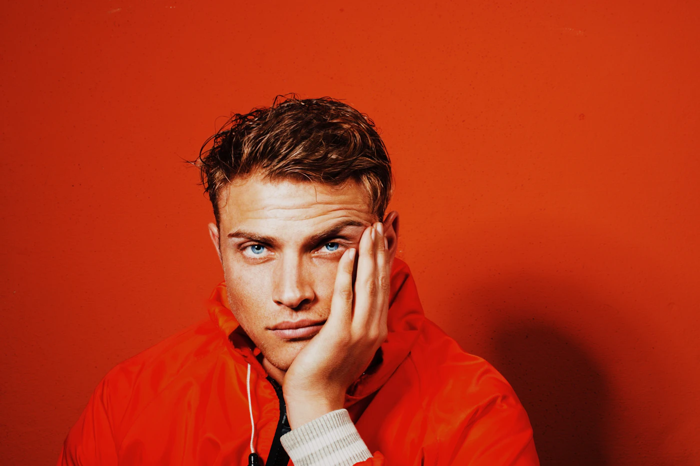 Man in an orange shell jacket posing against an orange backdrop