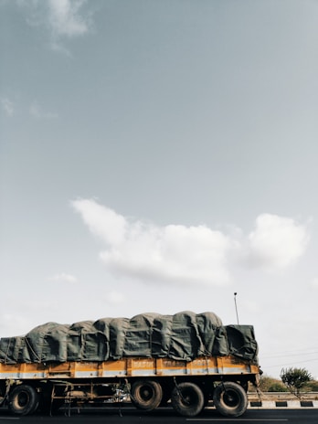 A large cargo truck loaded with various goods on a sunny highway.