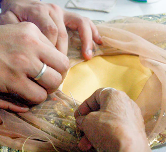 A serene studio shot of a skilled artisan hand-stitching a delicate garment in soft ivory fabric.