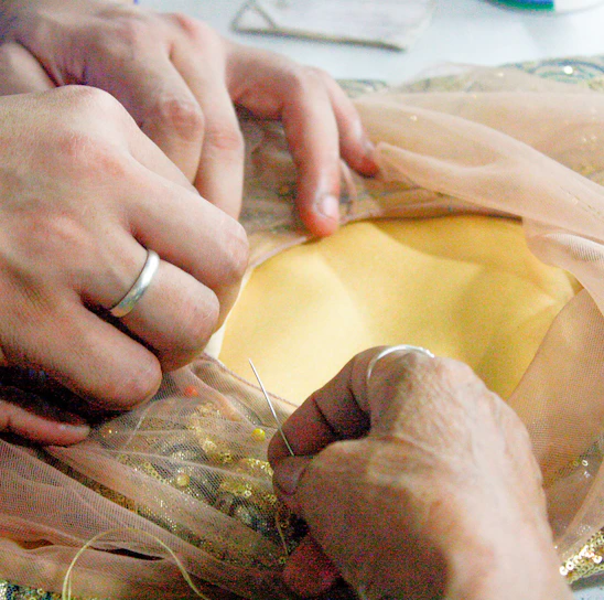 A serene studio shot of a skilled artisan hand-stitching a delicate garment in soft ivory fabric.