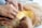 Hands are carefully sewing a piece of fabric, with one person holding a needle and thread while another adjusts delicate sheer material. The fabric beneath includes a mix of yellow and gold sequins, suggesting careful craftsmanship and attention to detail.