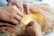 Hands are carefully sewing a piece of fabric, with one person holding a needle and thread while another adjusts delicate sheer material. The fabric beneath includes a mix of yellow and gold sequins, suggesting careful craftsmanship and attention to detail.