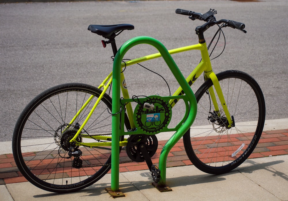 a yellow bicycle locked to a green bike rack