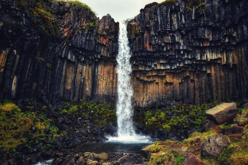 a waterfall is surrounded by rocks and greenery