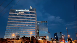 A sleek Mercedes billboard glowing brightly on a busy city street at dusk