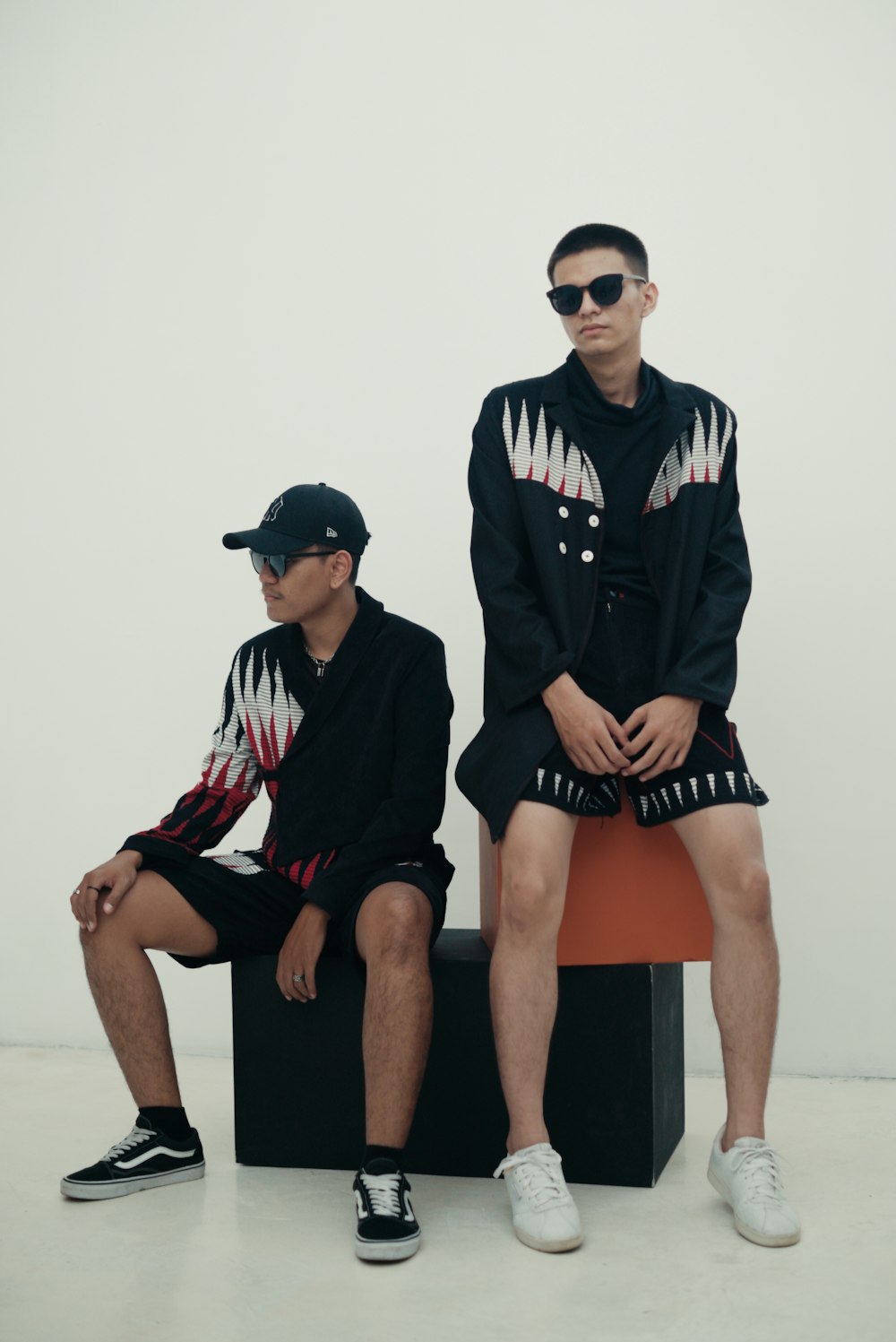 two young men sitting on a bench in front of a white wall