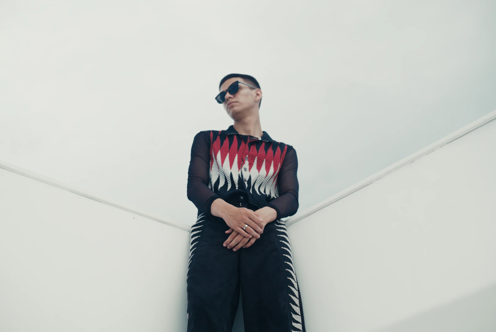 Model in a patterned black and red shirt against a white wall