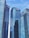 Tall modern skyscrapers with reflective glass facades dominate the scene, set against a clear blue sky. Each building features logos of various financial institutions.