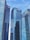 Tall modern skyscrapers with reflective glass facades dominate the scene, set against a clear blue sky. Each building features logos of various financial institutions.