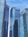 Tall modern skyscrapers with reflective glass facades dominate the scene, set against a clear blue sky. Each building features logos of various financial institutions.