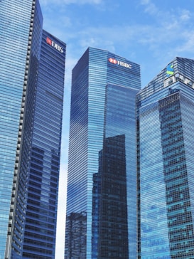 Tall modern skyscrapers with reflective glass facades dominate the scene, set against a clear blue sky. Each building features logos of various financial institutions.