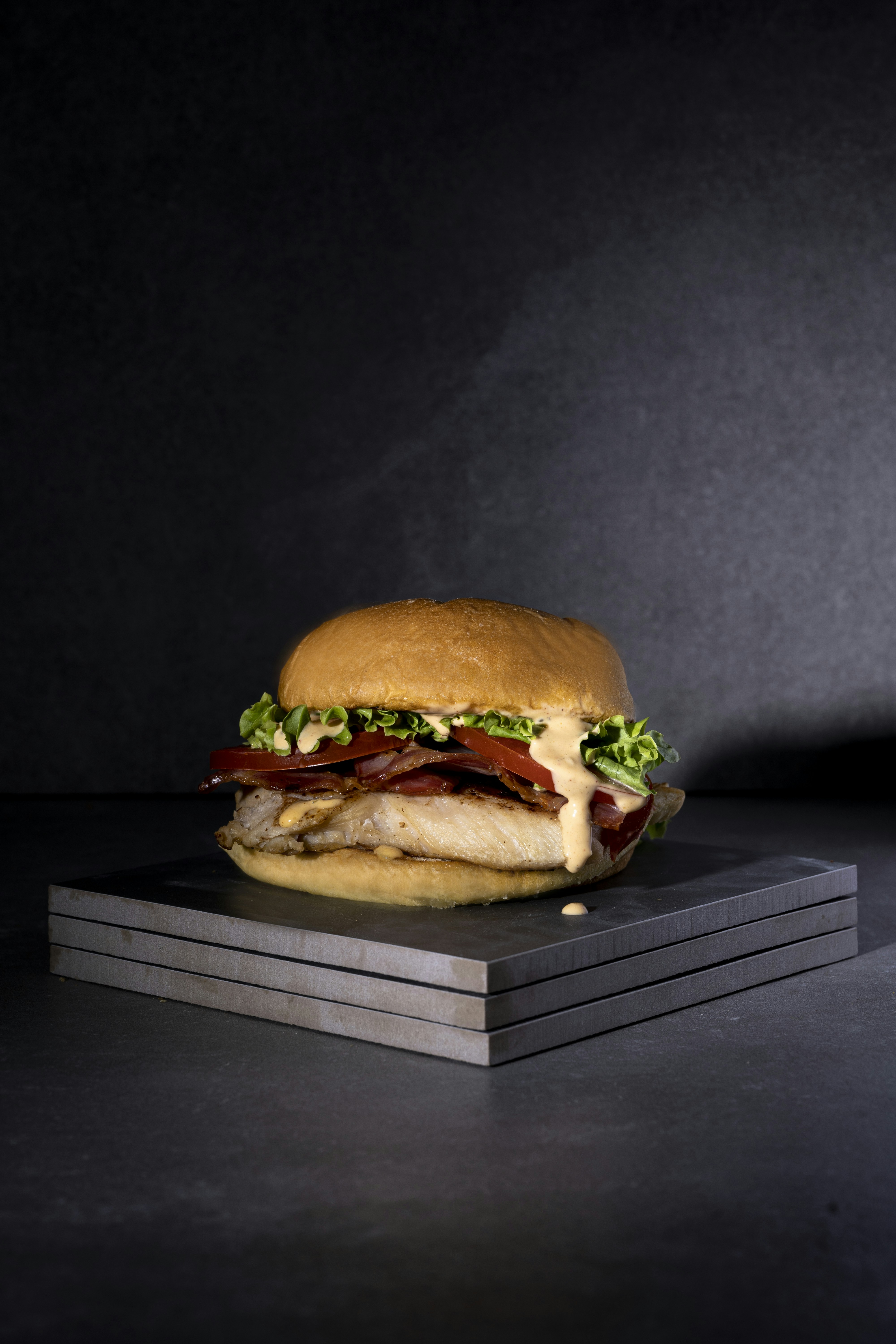 Gourmet burger stacked high on dark board, dramatic dark background, moody lighting