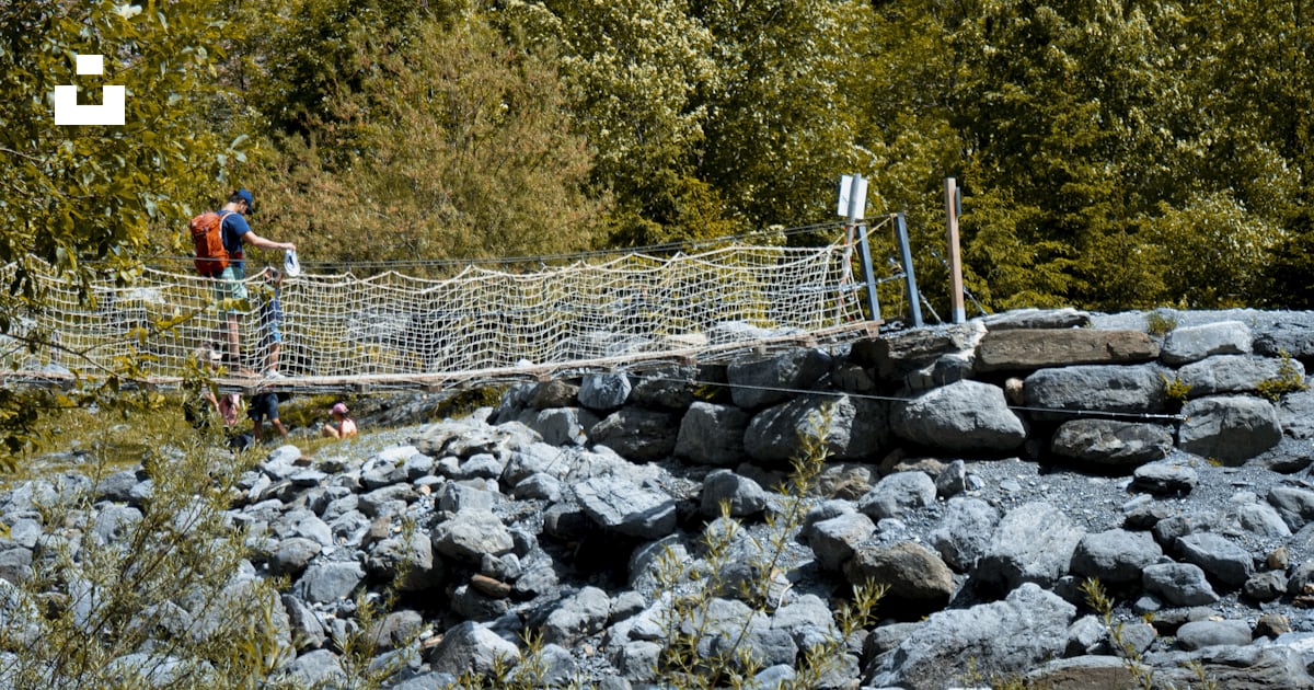A couple of people walking across a bridge over rocks photo – Free ...