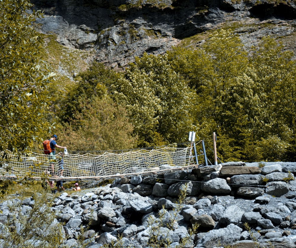 a couple of people walking across a bridge over rocks